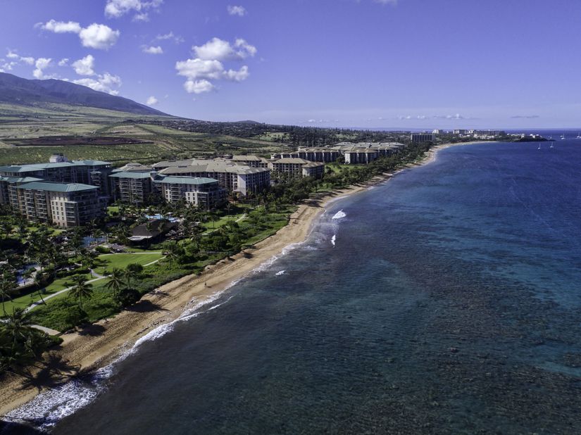 aerial-view-of-kaanapali-beach-with-its-white-sandy-beaches-lined-by-palm-trees-and-rows-of-resorts-surrounded-by-crystal-clear-blue-water