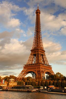 View of the iconic Eiffel Tower at sunset, boats sit at the piers at the base of the landmark, its ironwork turned orange by the setting sun