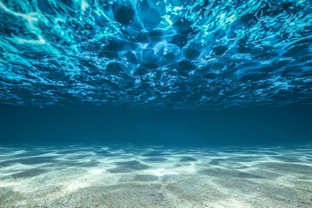 Photo of the ocean bottom with white sandy floor deep blue water and waves above