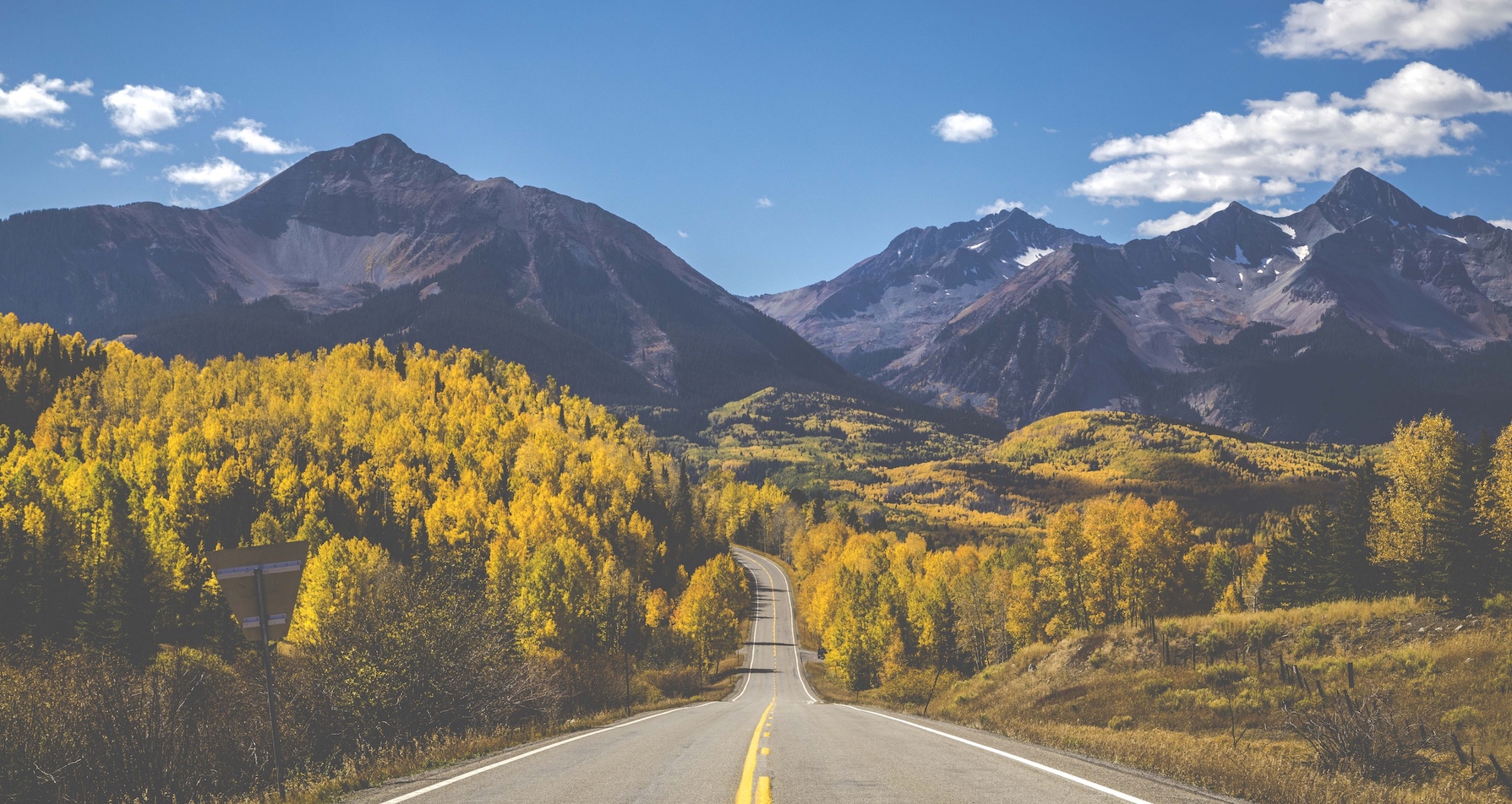 A two lane road through a mountain forest in the fall