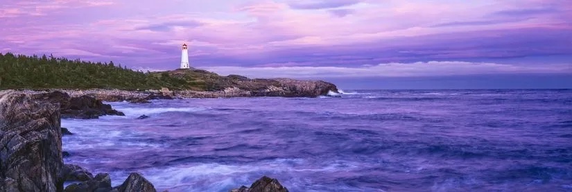 A rocky shoreline with a white lighthouse at sunset