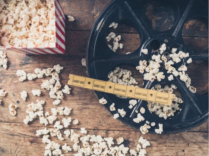 Classic box of popcorn with spilled popcorn on an empty movie reel with movie tickets